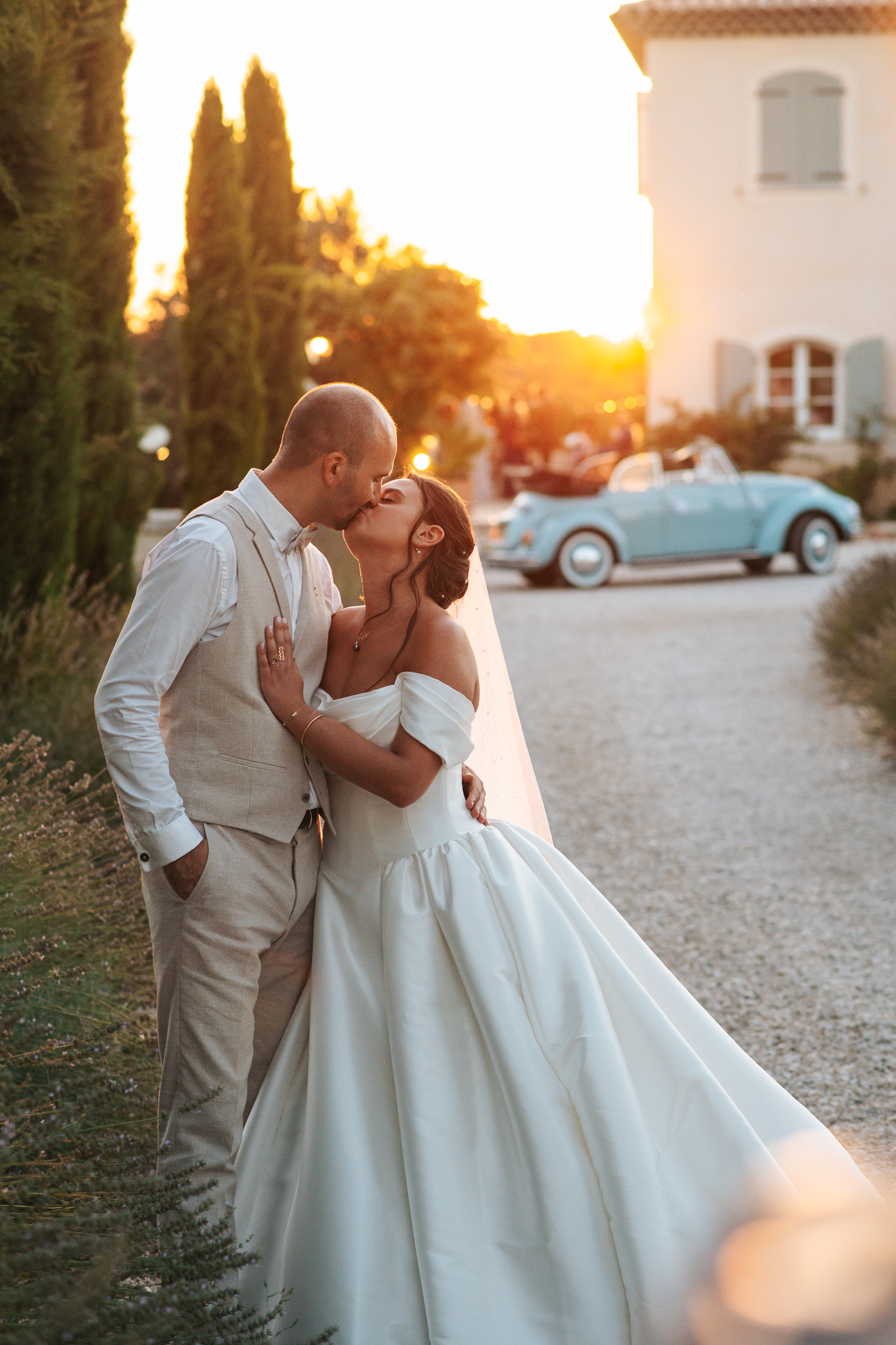 Un couple s'embrasse devant une voiture ancienne, au coucher du soleil
