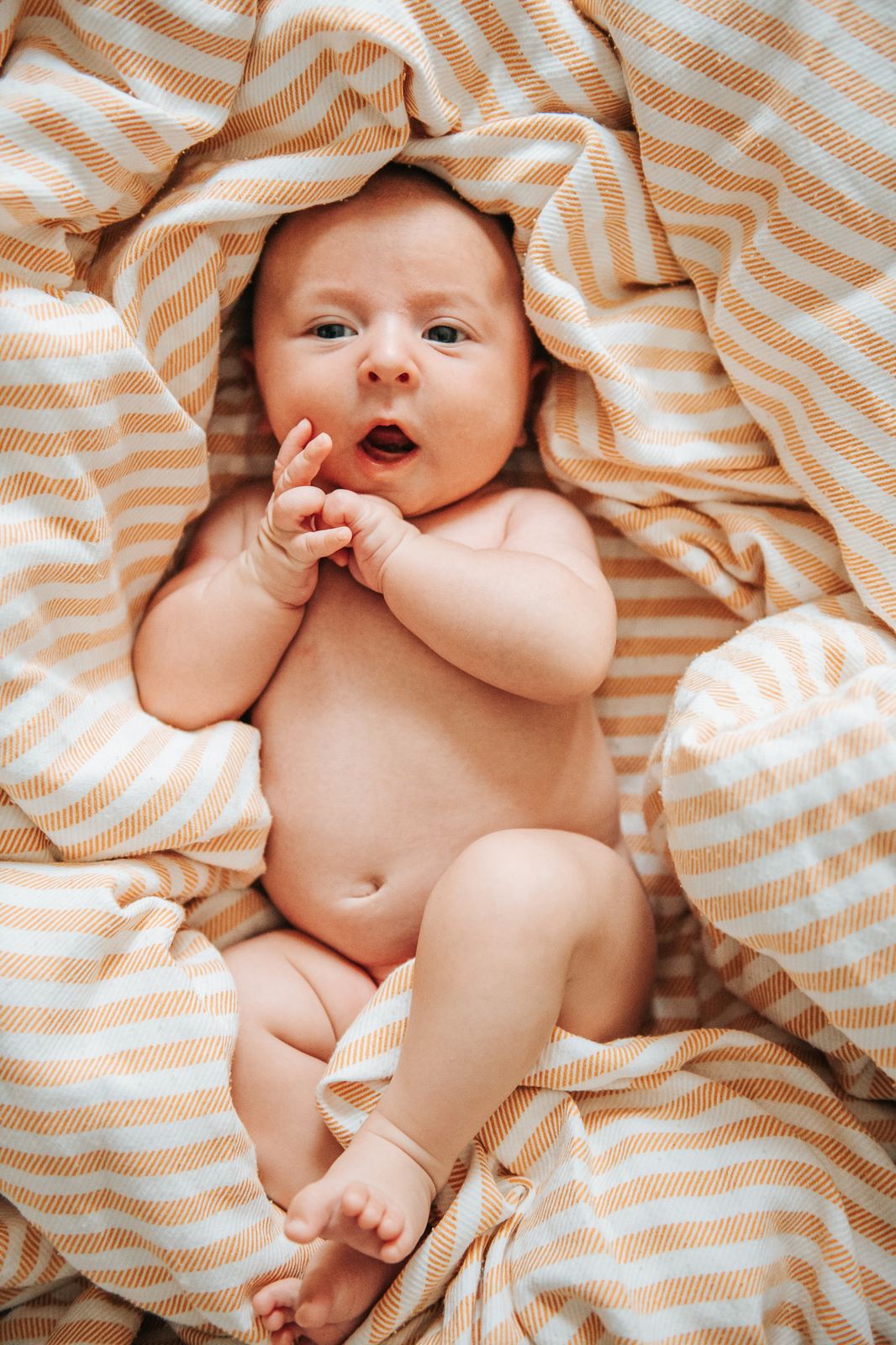 Bébé bien réveillé qui regarde l'objectif, allongé sur un drap rayé
