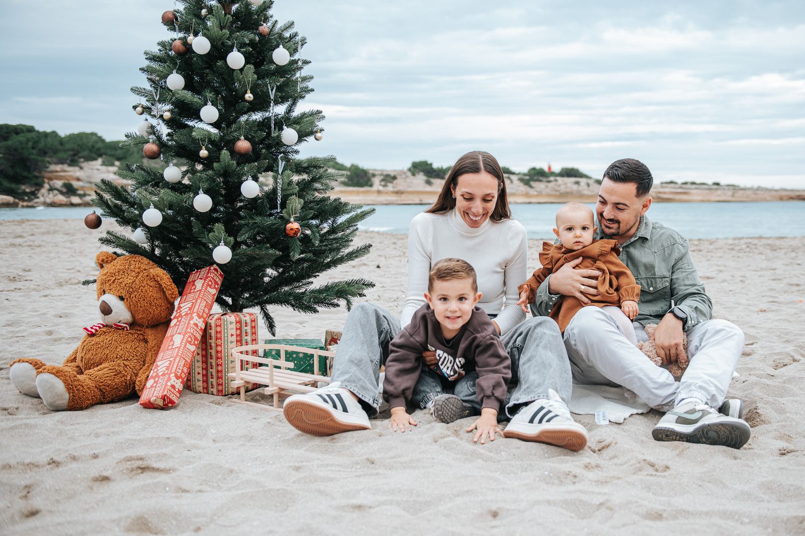 Famille sur la plage en hiver, à côté d'un sapin et d'un ours en peluche