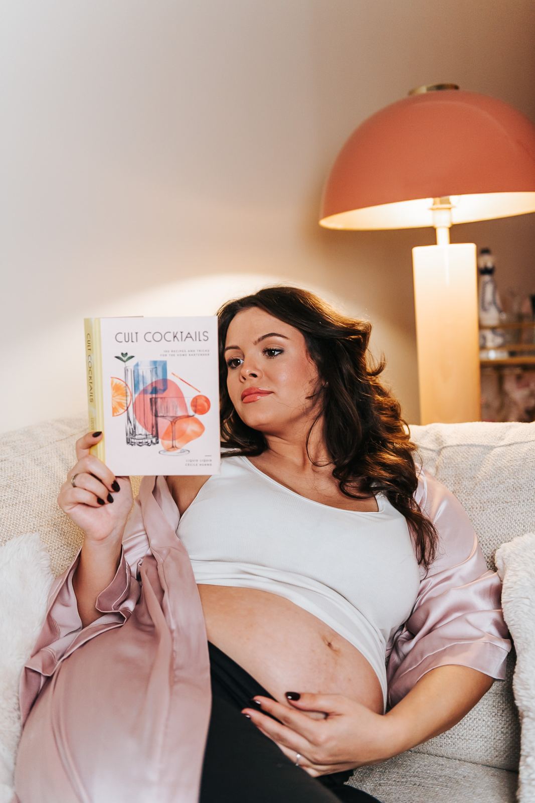 Future maman installée dans son canapé avec un livre, chez elle