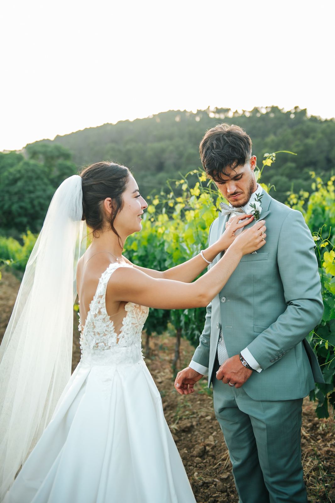 La mariée ajuste la boutonnière du marié dans les vignes