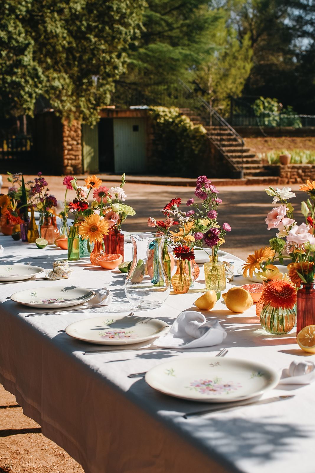 Grande table de mariage dressée sous les arbres avec des fleurs colorées