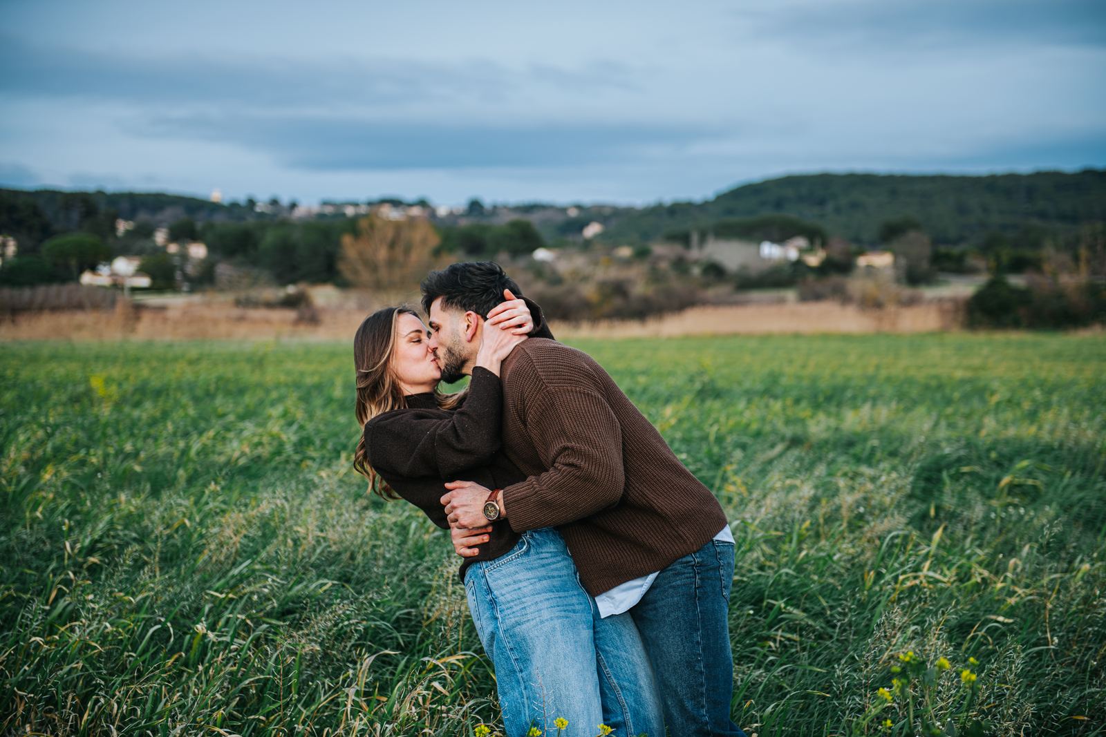 Couple qui s'embrasse dans un champ sous un ciel gris