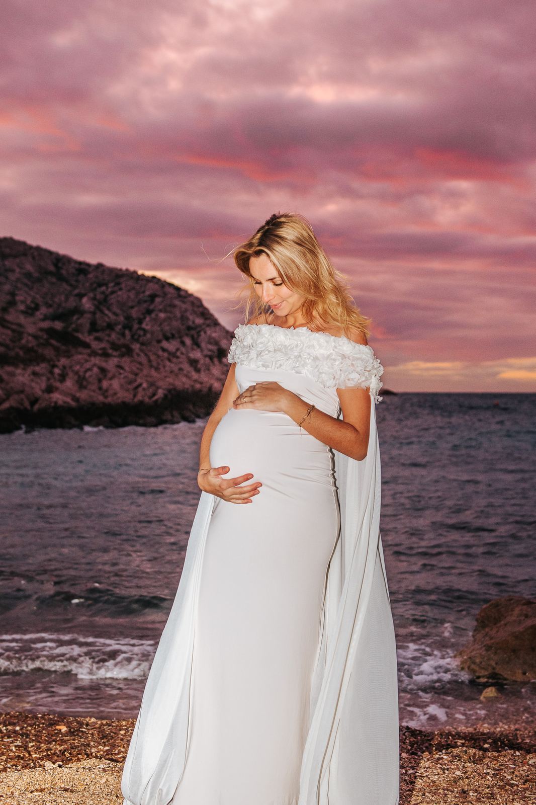 Future maman face à la mer sous un ciel rose et chargé