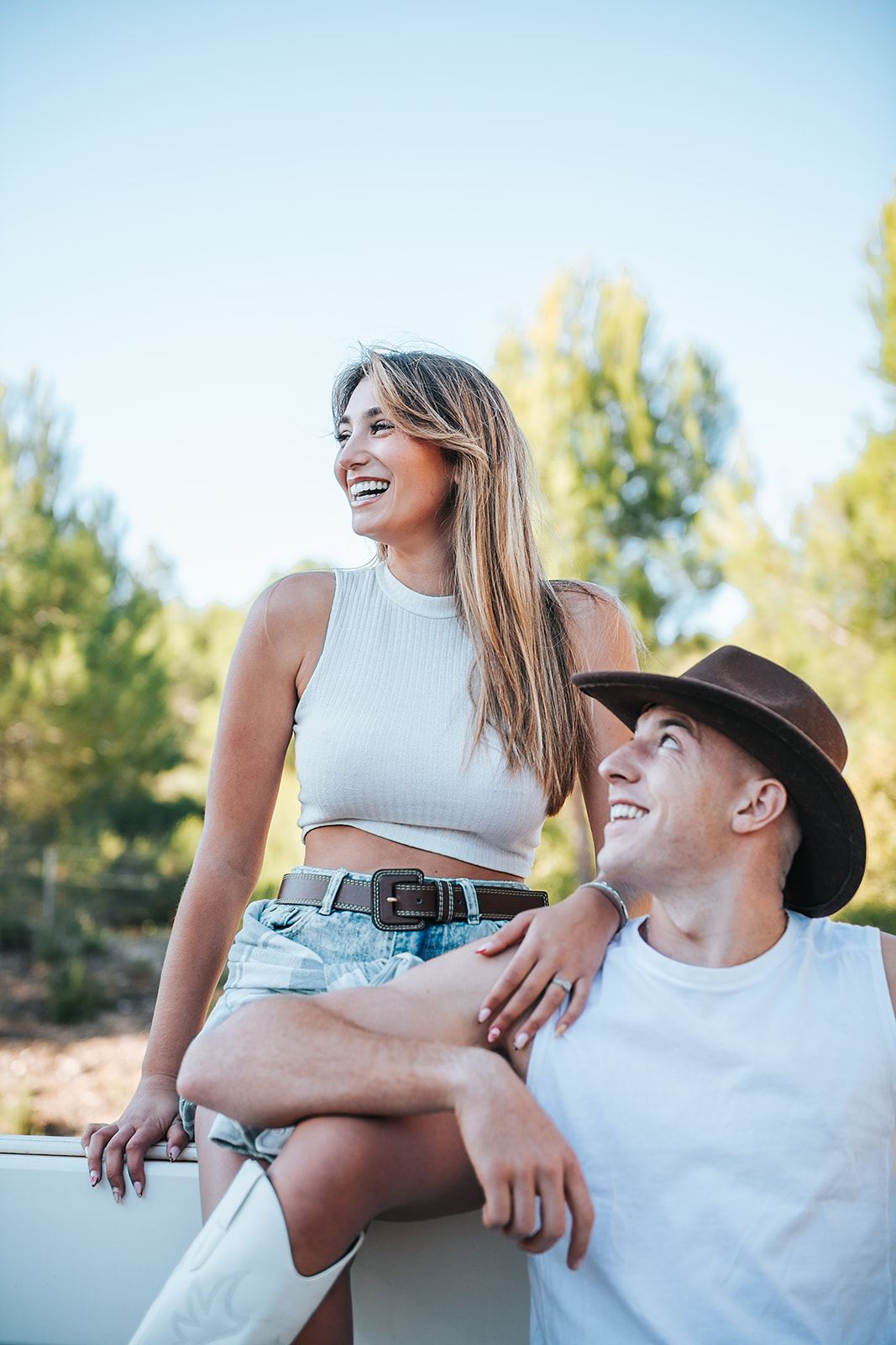 Couple qui rit, elle assise sur une barrière blanche