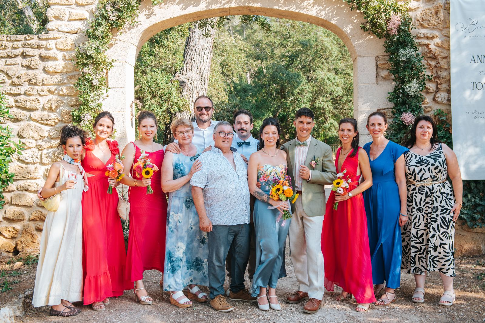 Photo de groupe souriante avec les proches des mariés, sous une arche en pierre