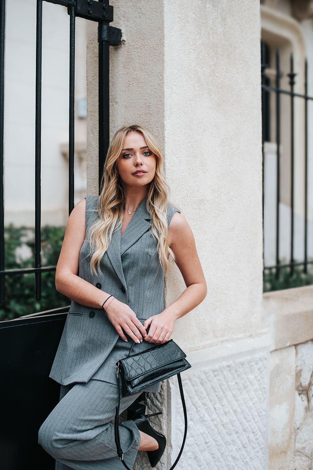 Femme en ensemble gris appuyée contre une façade en pierre