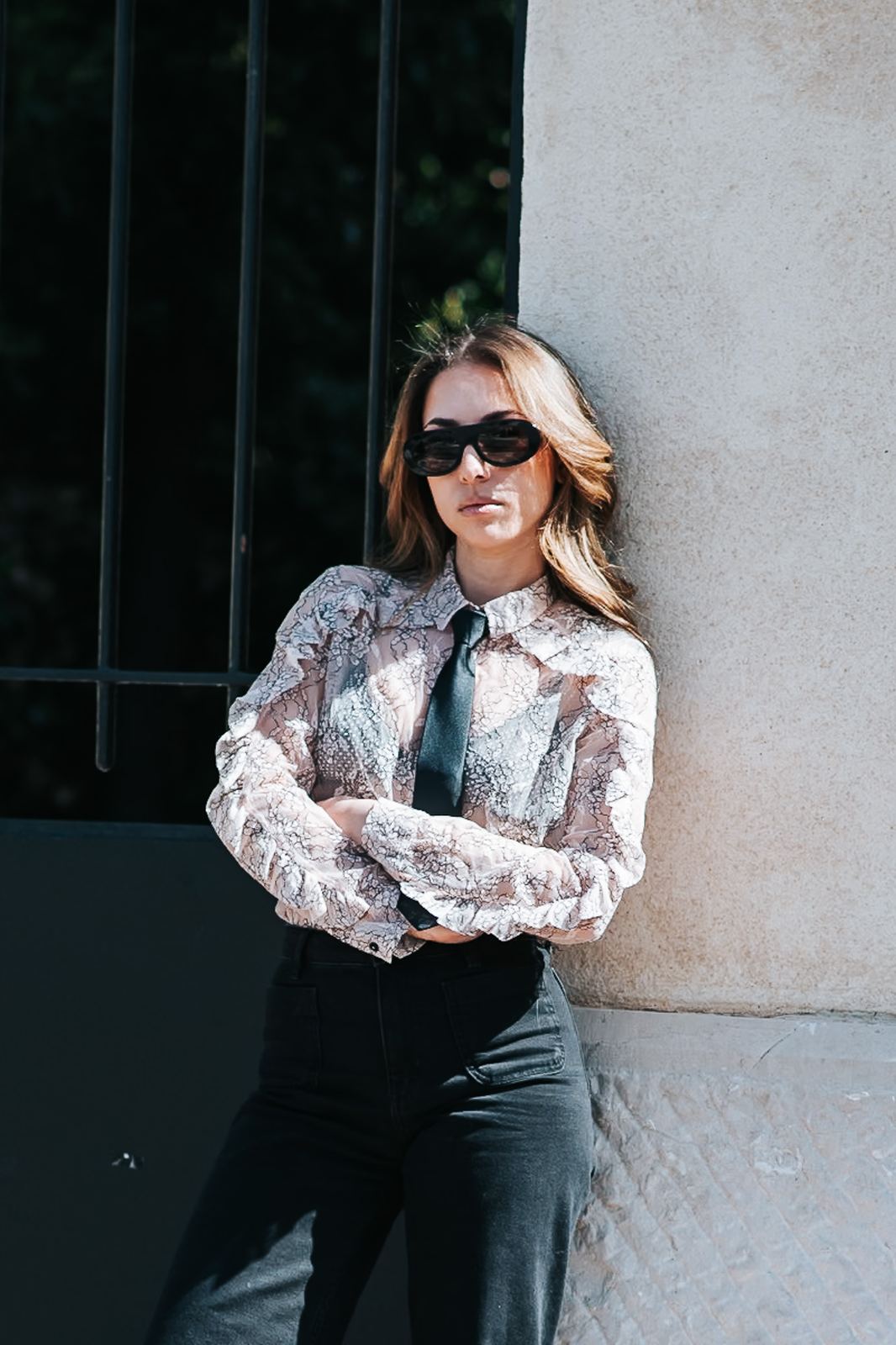 Femme en chemisier à motifs et pantalon noir devant une grille