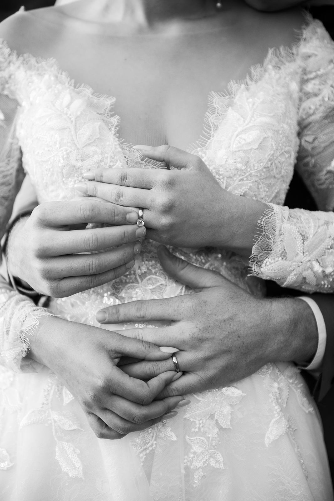 Mains des mariés enlacées sur la robe, en noir et blanc