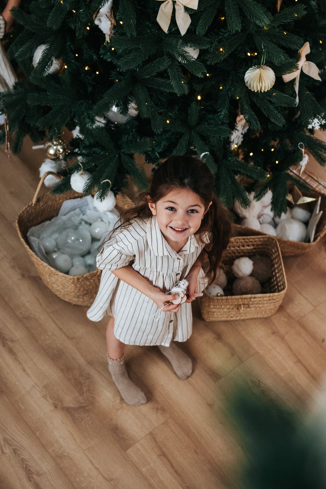 Petite fille qui rit, assise sous le sapin de Noël