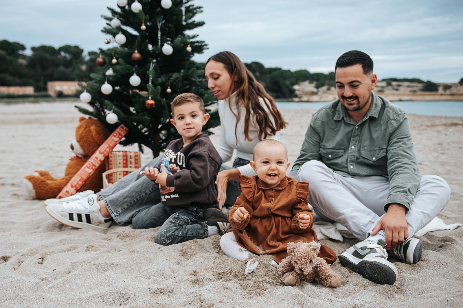 Famille assise sur la plage à côté d'un sapin de Noël, tout le monde regarde l'objectif