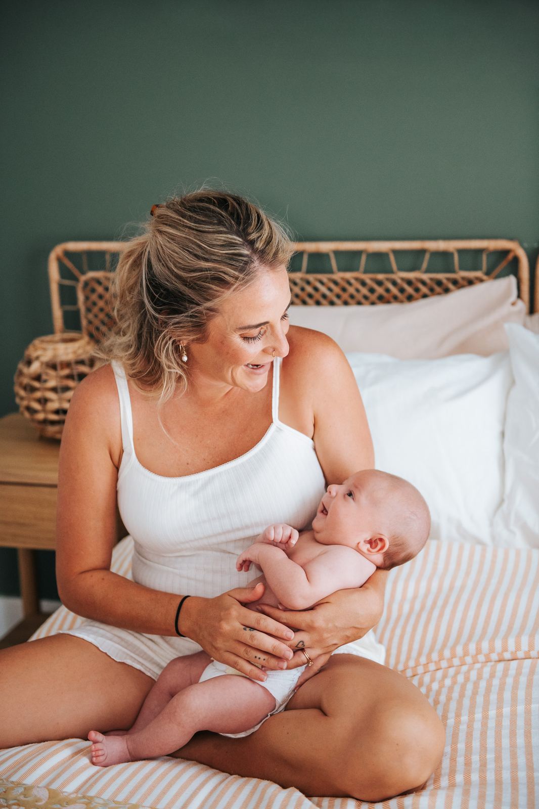 Maman assise sur son lit avec son bébé, dans une chambre lumineuse
