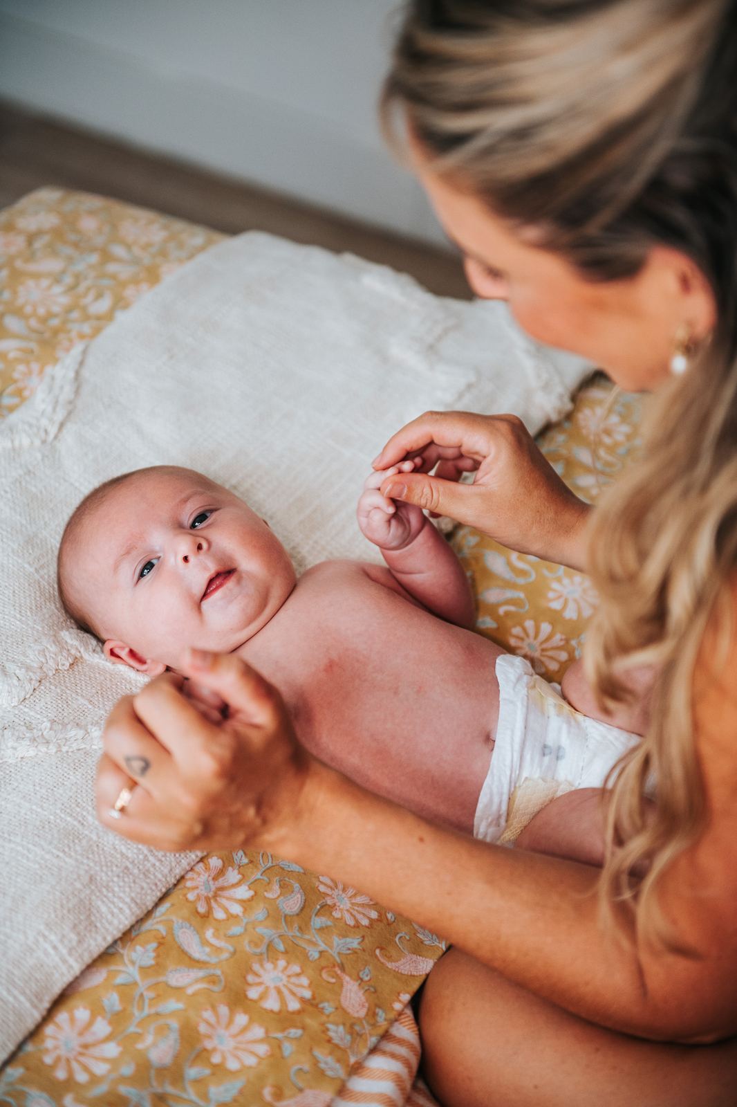 Maman qui change son bébé sur le lit en souriant