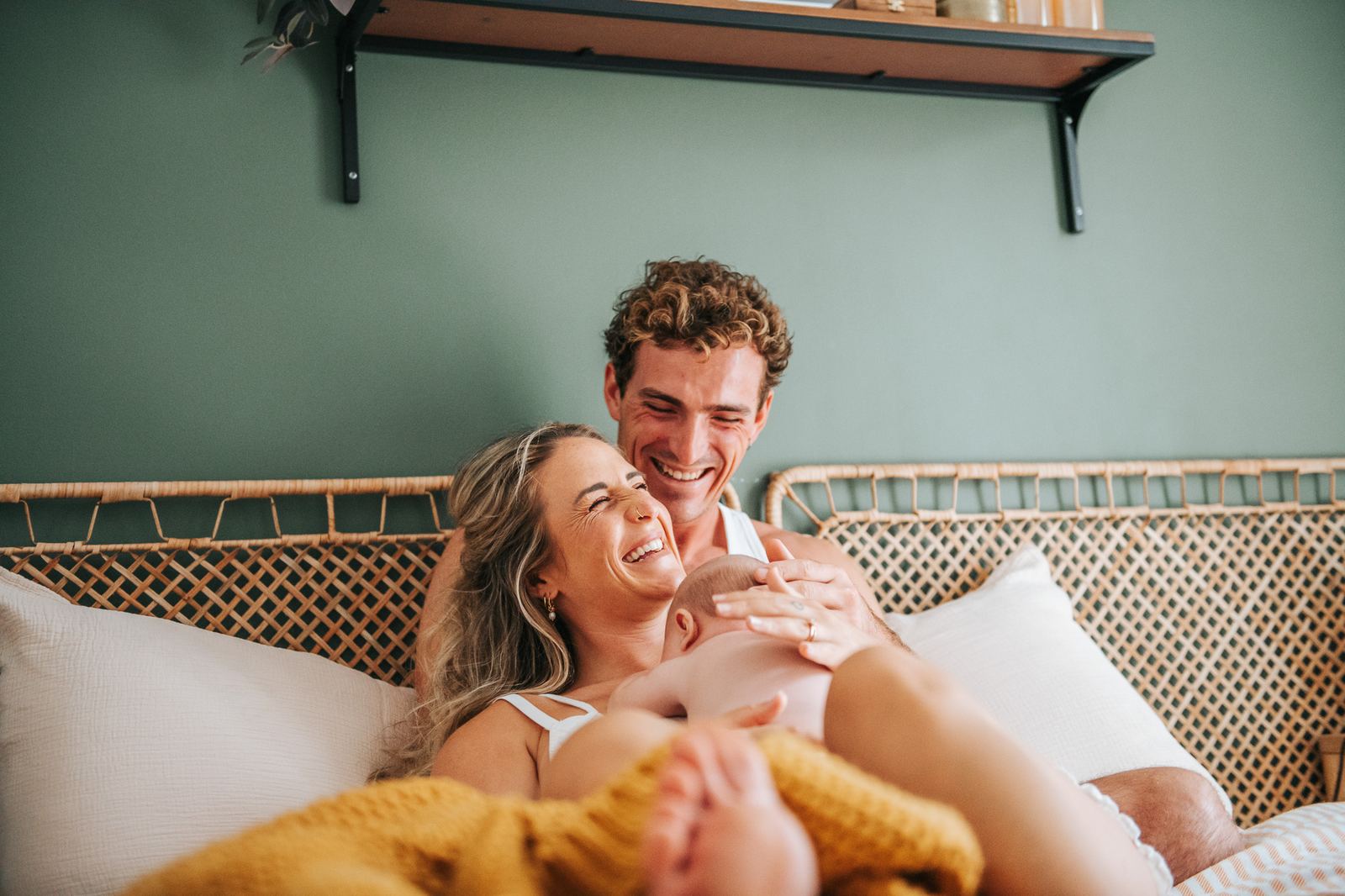 Parents qui rient sur leur lit avec leur nouveau-né