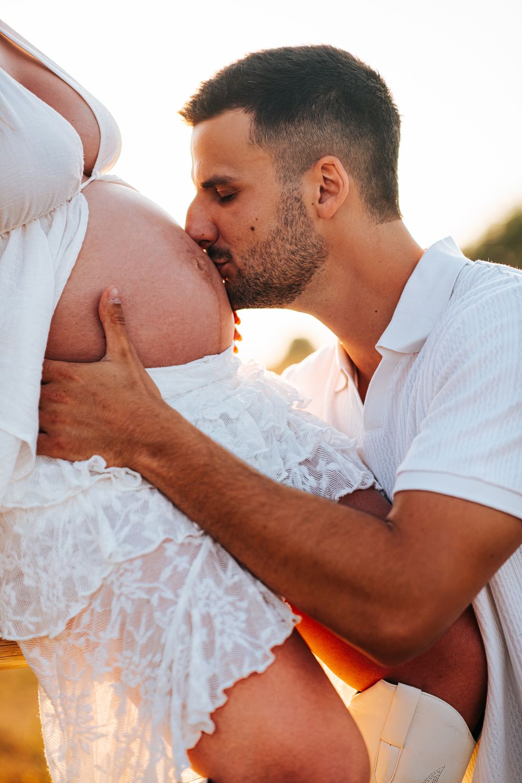 Futur papa qui embrasse le ventre de sa compagne en contre-jour