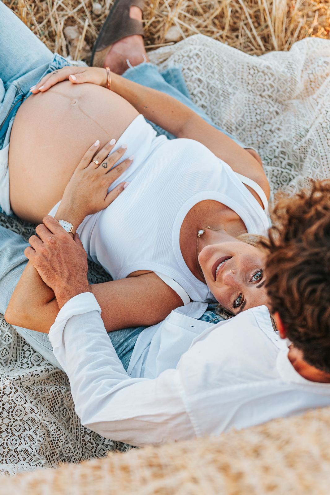 Couple allongé dans la paille qui rit, ventre de grossesse au premier plan
