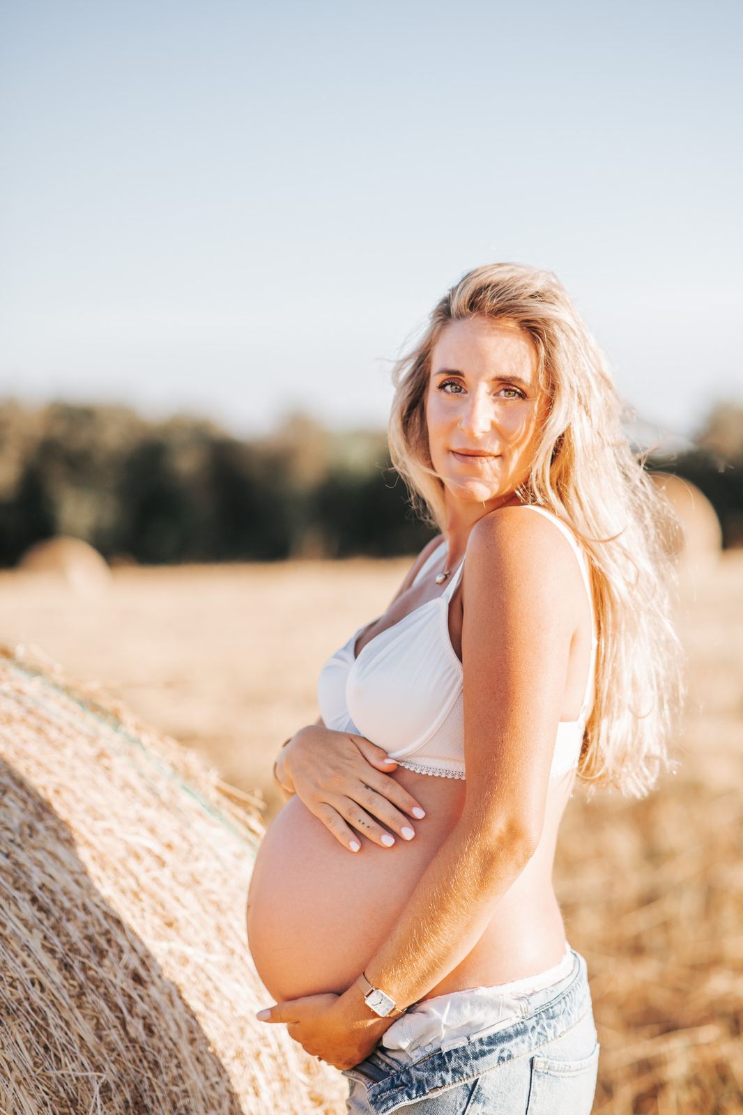 Future maman appuyée contre une botte de paille, main sur le ventre