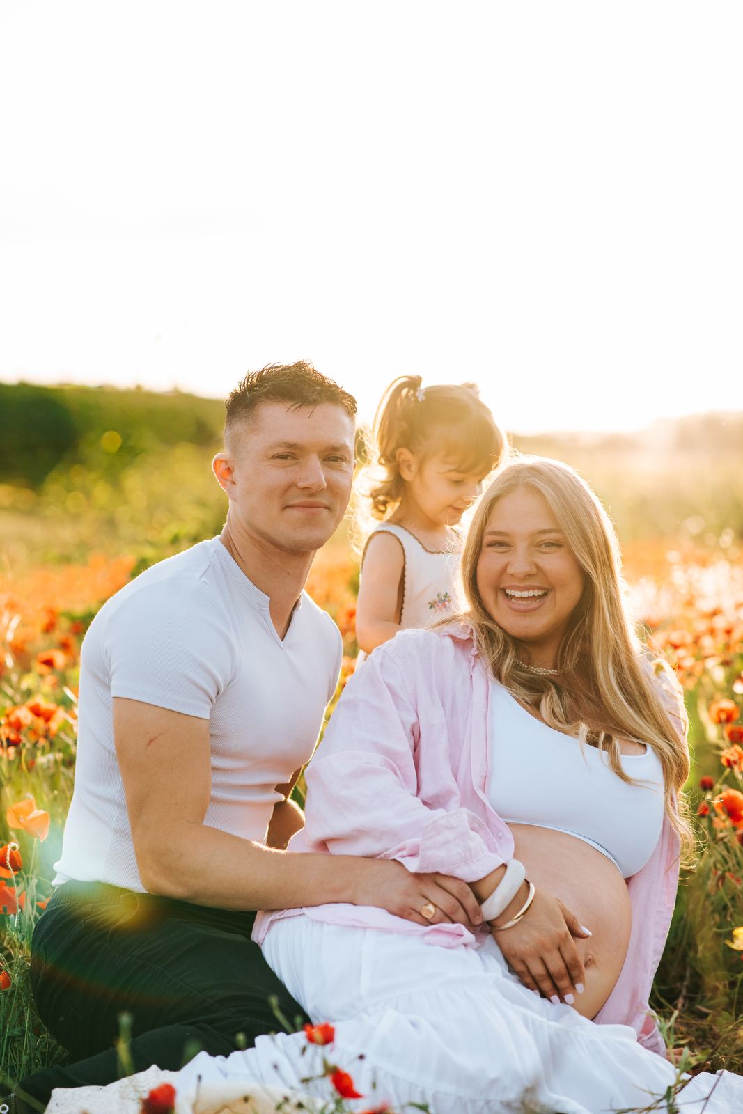 Couple et leur fille assis dans les coquelicots en fin de journée