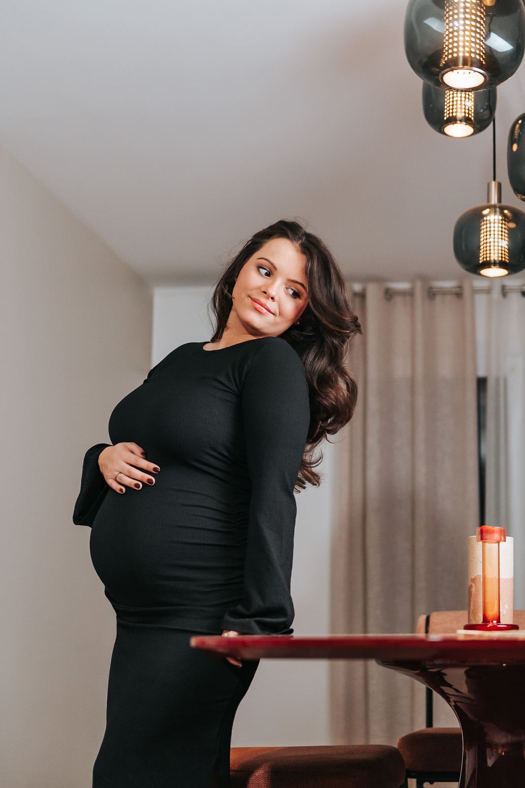 Future maman en robe longue en maille noire près du corps, chez elle
