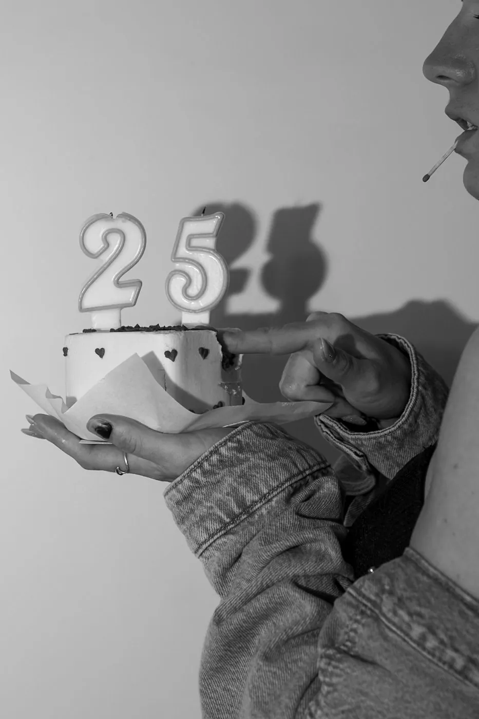 Anniversaire 25 ans : jeune femme qui goûte la crème de son gâteau, bougies 2 et 5 et leur ombre au mur, en noir et blanc