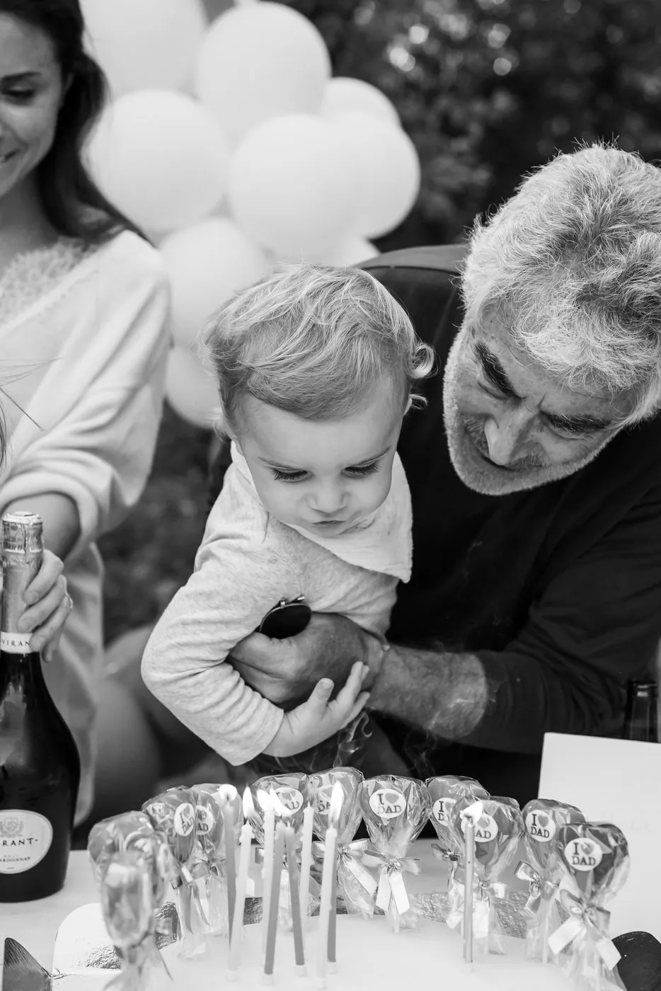 Grand-père tenant son petit-fils au-dessus des bougies d'un gâteau d'anniversaire, en noir et blanc