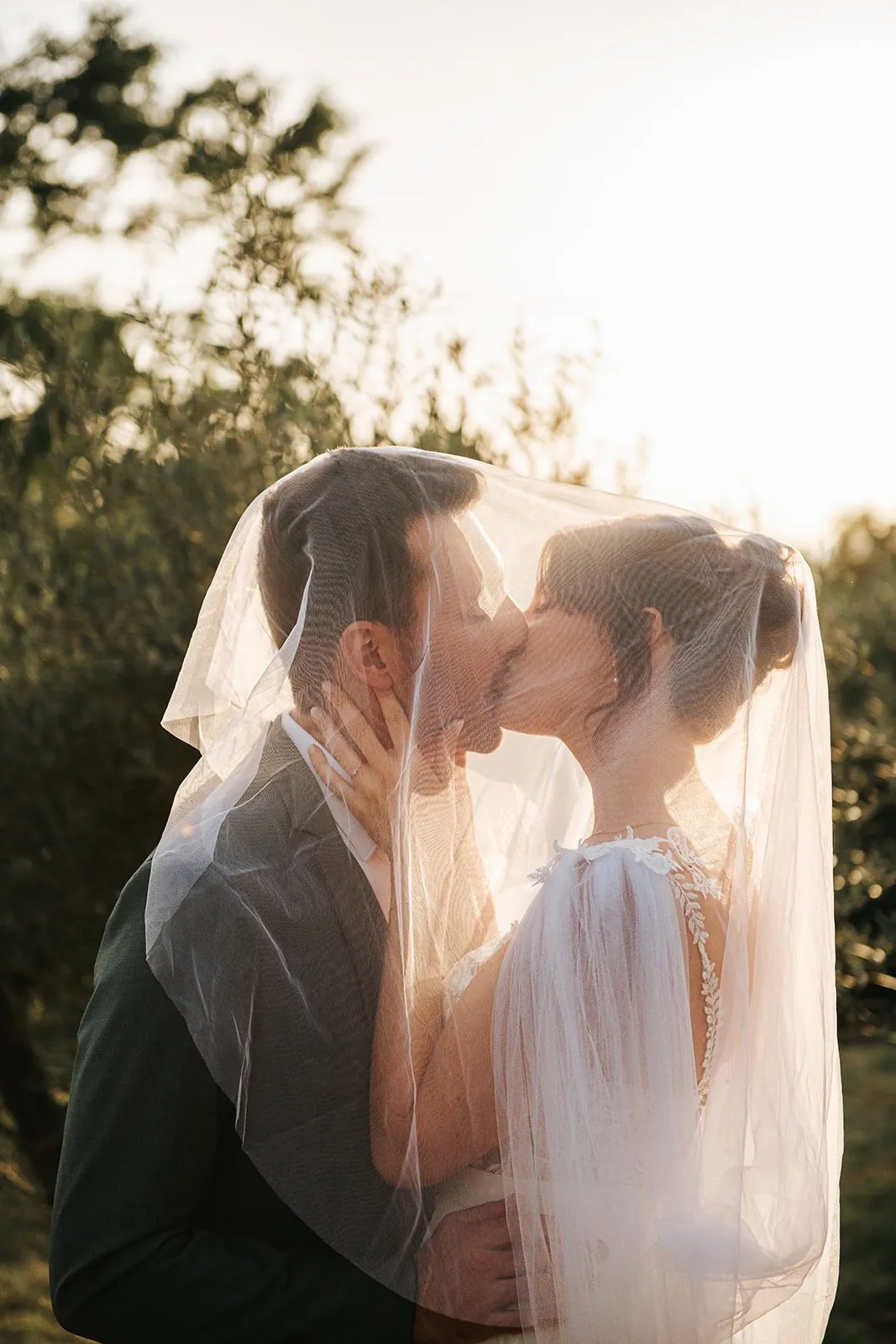 Mariage : baiser des mariés sous le voile, en contre-jour dans la lumière dorée de fin de journée