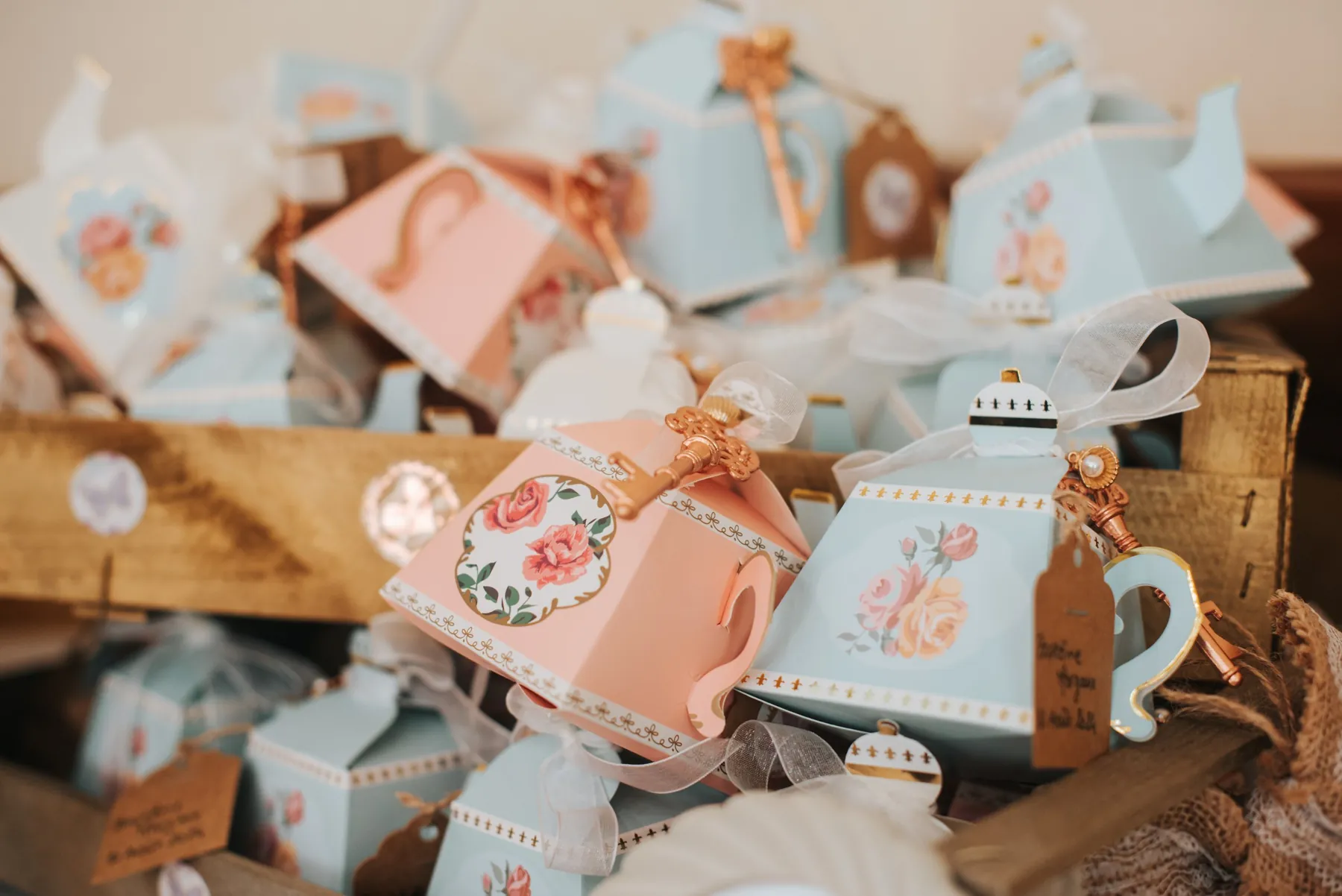 Détail de baptême : boîtes à dragées en forme de théières roses et bleues, décorées de roses et de clés dorées