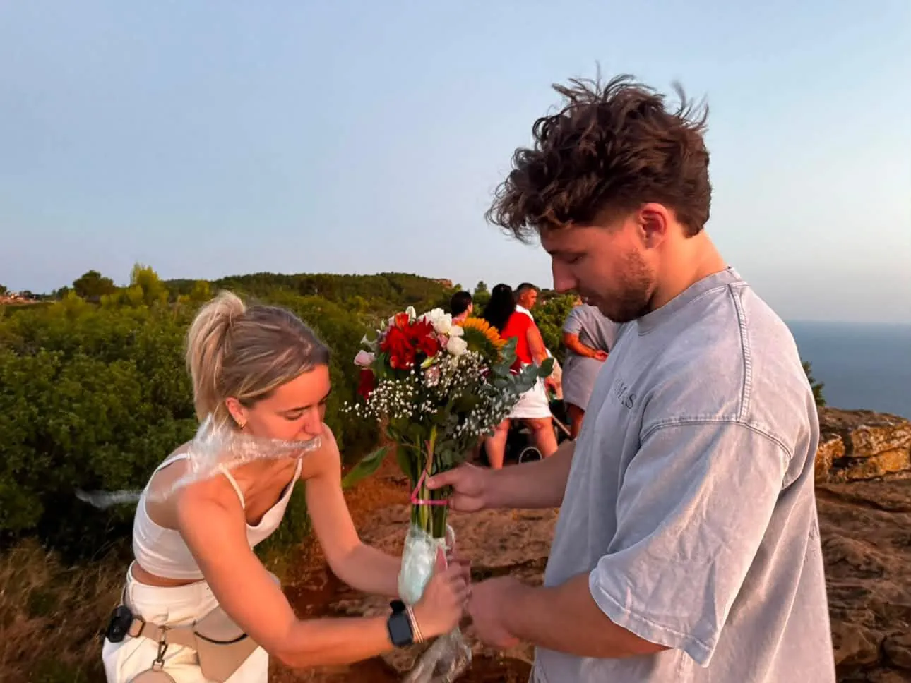 Coulisses d'une demande en mariage : préparation du bouquet de fleurs sur une falaise au-dessus de la mer