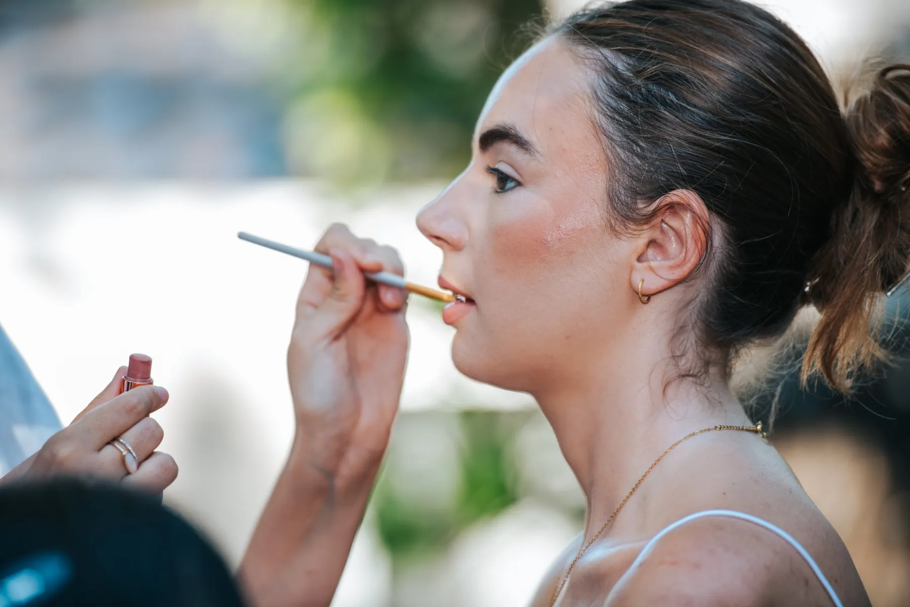 Coulisses d'événement : jeune femme de profil pendant sa mise en beauté, rouge à lèvres appliqué au pinceau
