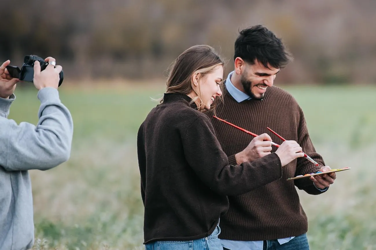 Coulisses d'une séance couple : ils rient en peignant ensemble, l'appareil photo en action au premier plan