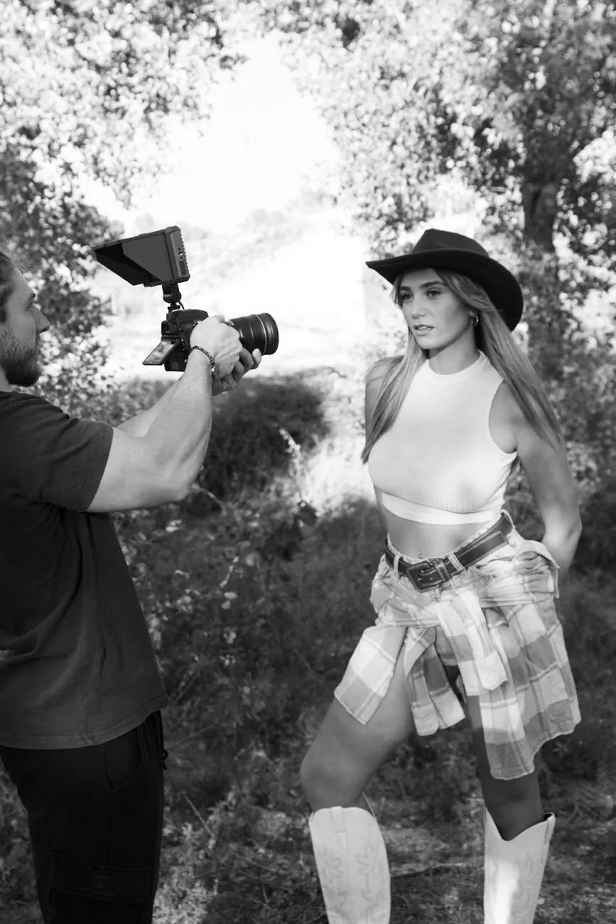 Coulisses en noir et blanc : un vidéaste filme une jeune femme en chapeau et bottes de cowboy