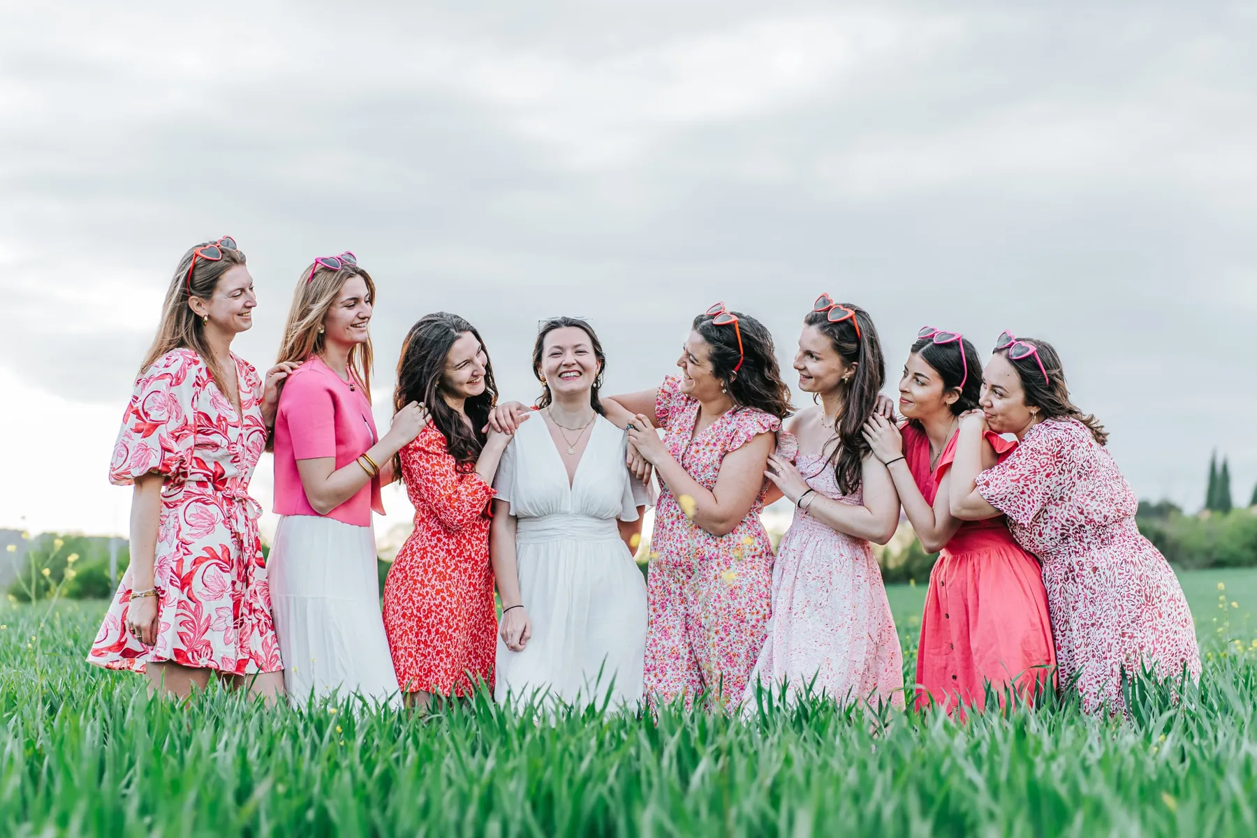 Enterrement de vie de jeune fille : la future mariée en robe blanche entourée de huit amies en rose, dans un champ