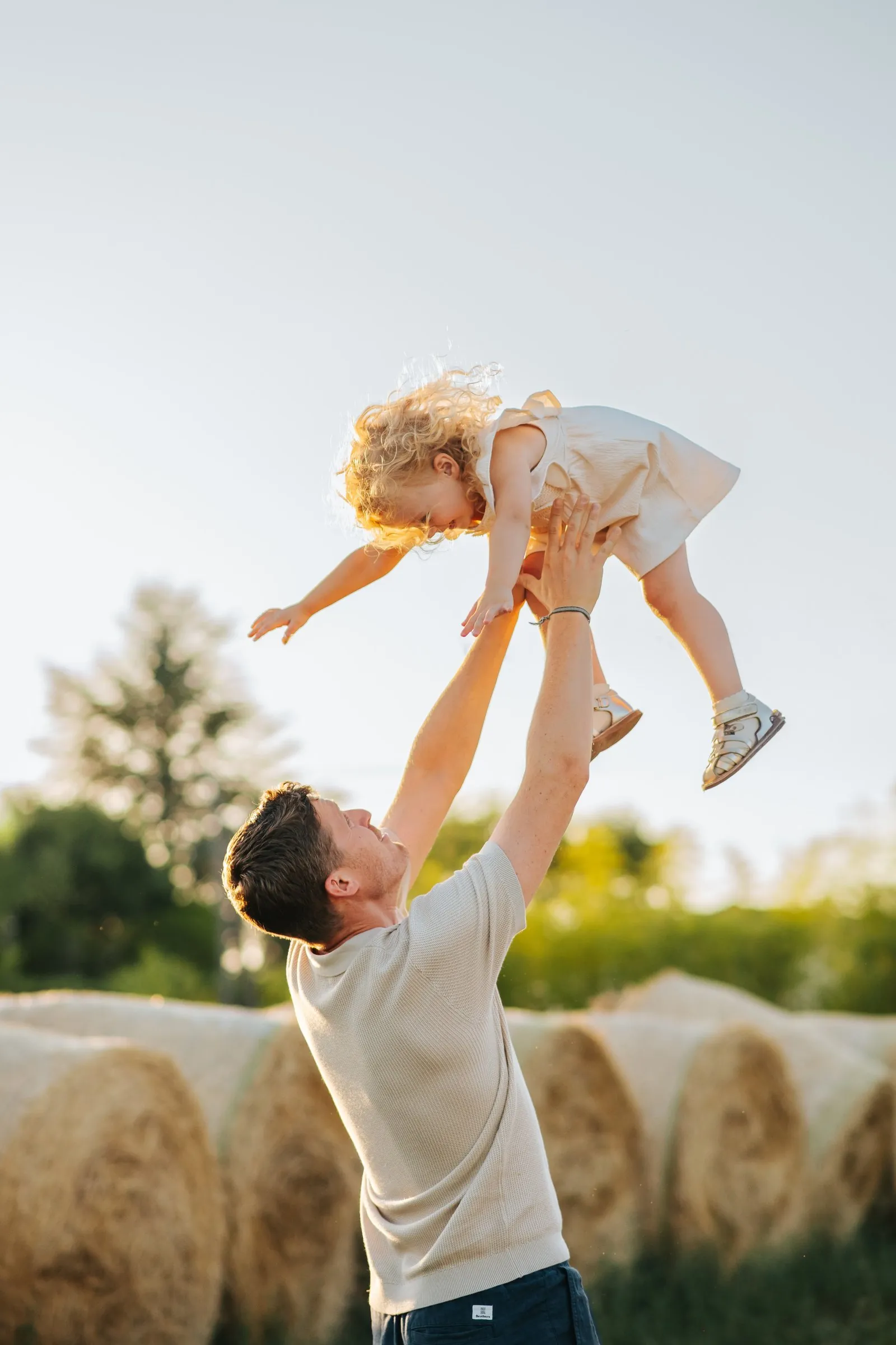Éclats de rire en famille : un père fait voler sa fille dans les airs, au milieu des champs et des bottes de paille