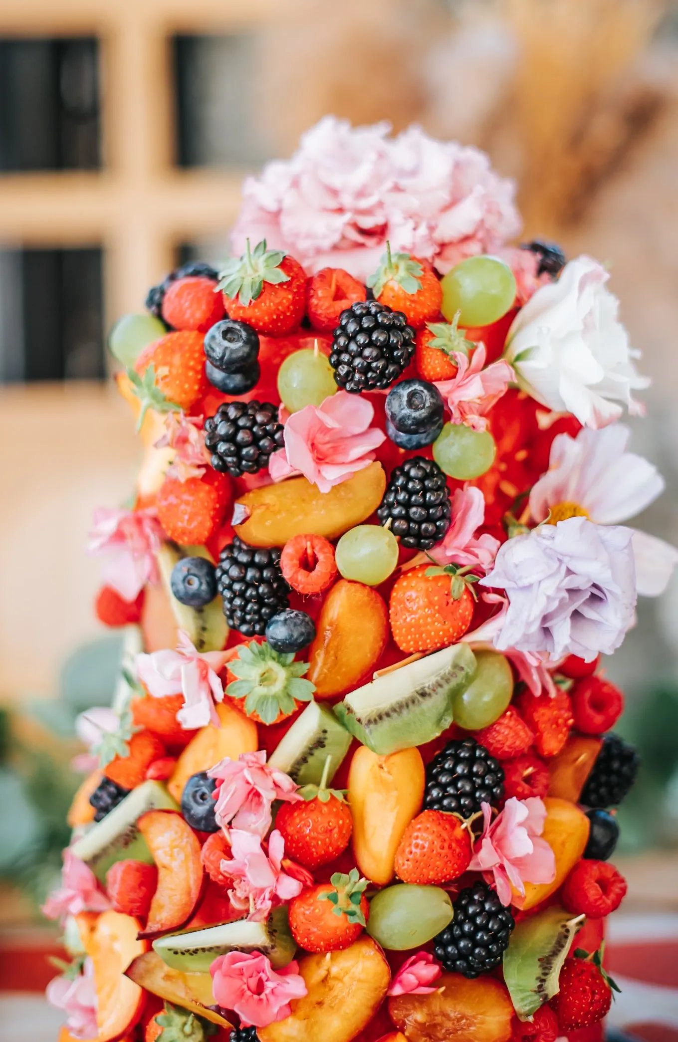 Détail d'événement : gâteau recouvert de fruits frais, fraises, mûres, myrtilles et fleurs roses comestibles