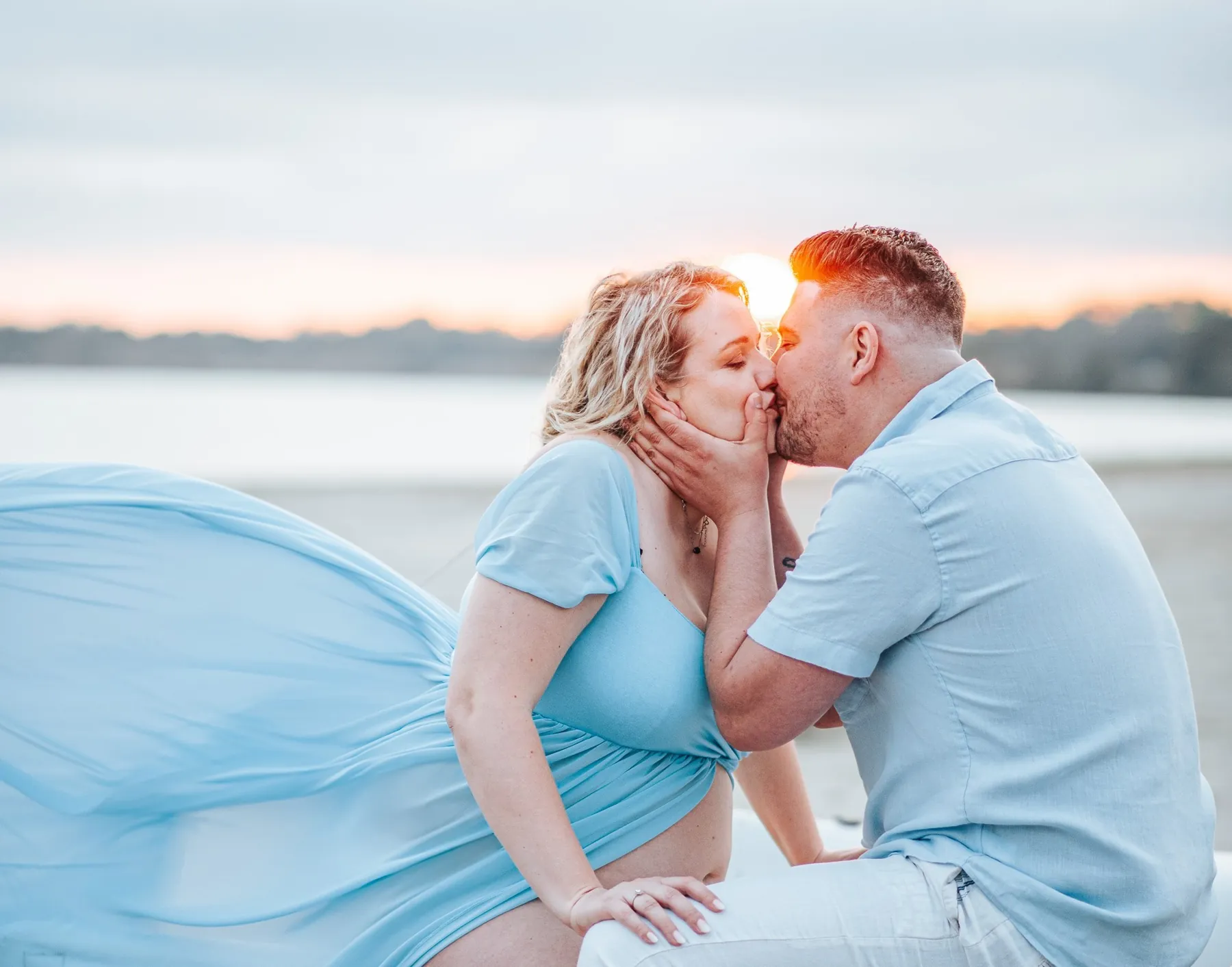 Séance grossesse au bord de l'eau près de Montpellier : un baiser, la robe bleue au vent