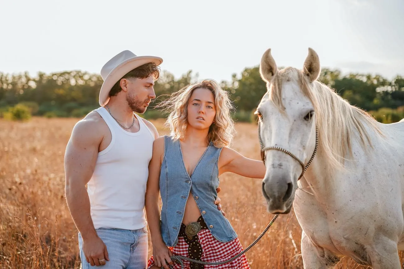 Léna et Thomas en tenue western dans un champ d'herbes dorées, aux côtés d'un cheval blanc