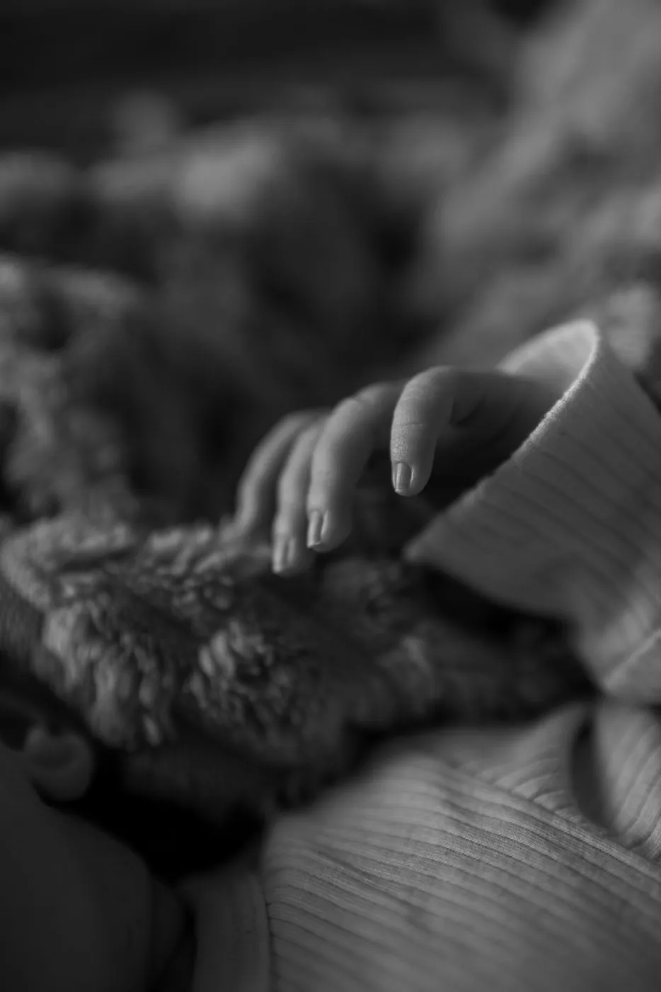 Séance bébé à domicile : petite main de nouveau-né posée sur une couverture moelleuse, détail en noir et blanc