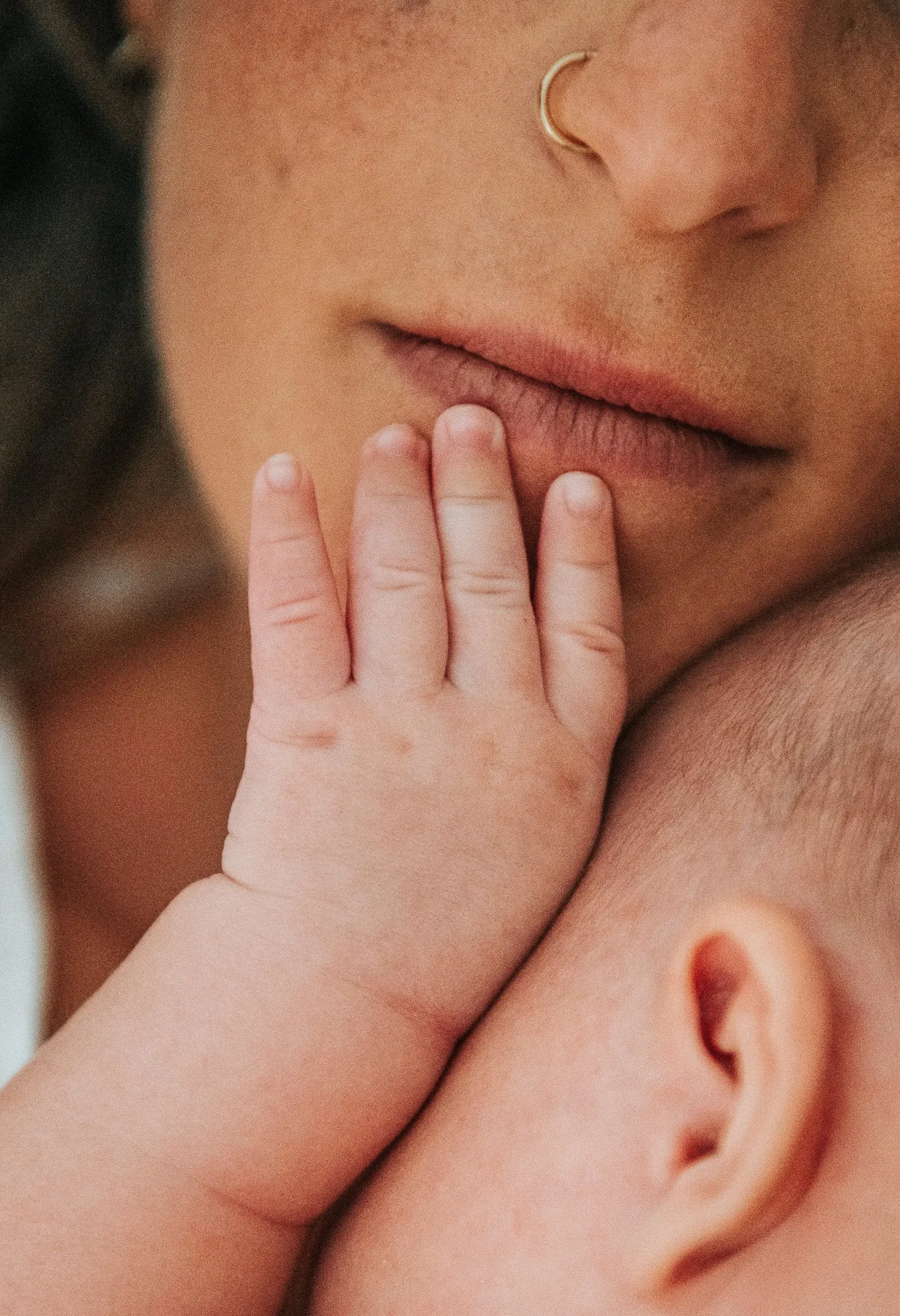 Séance nouveau-né : petite main de bébé posée sur les lèvres de sa maman, gros plan doux et intime