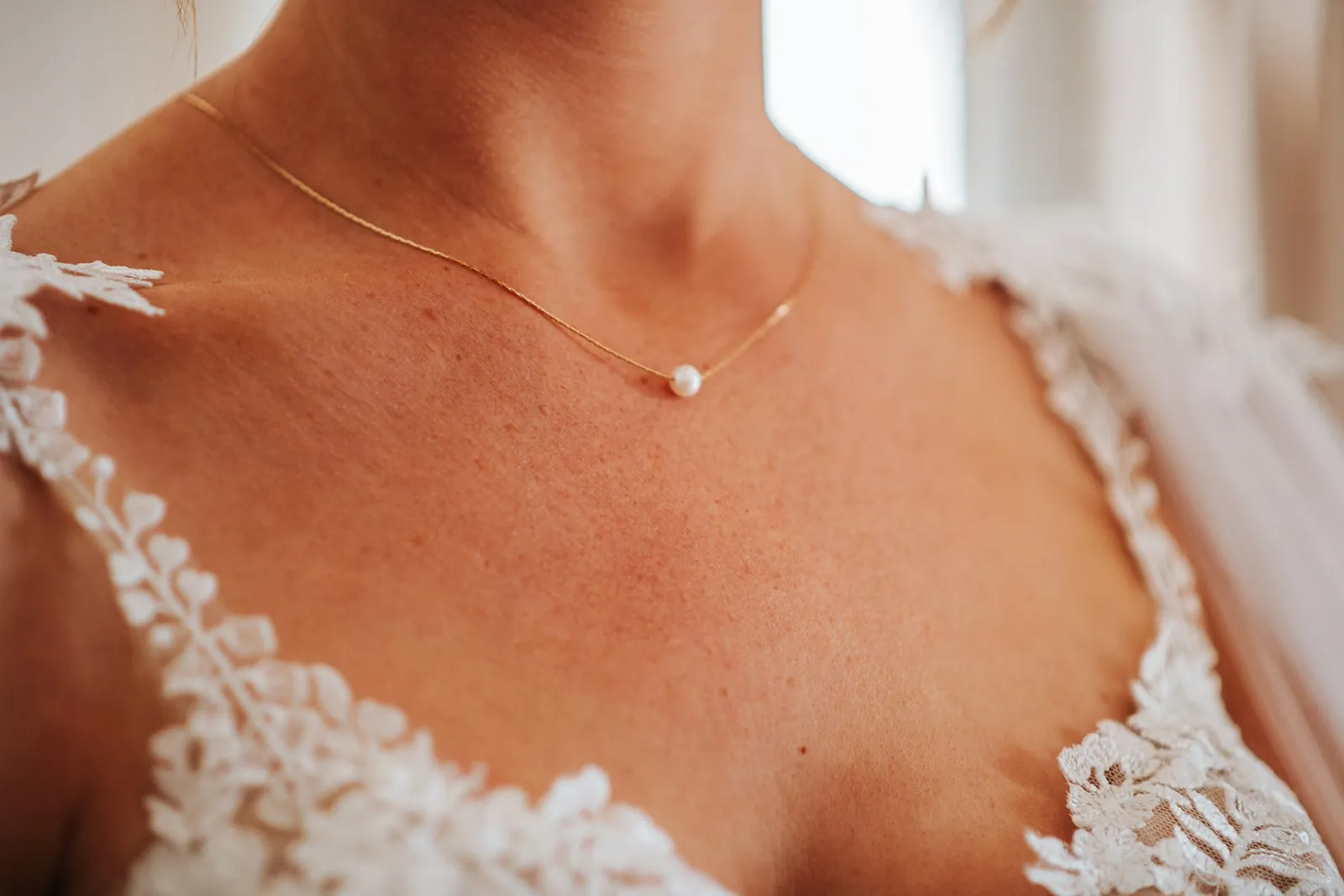 Détail de mariage : fin collier doré à une perle sur le décolleté en dentelle de la mariée