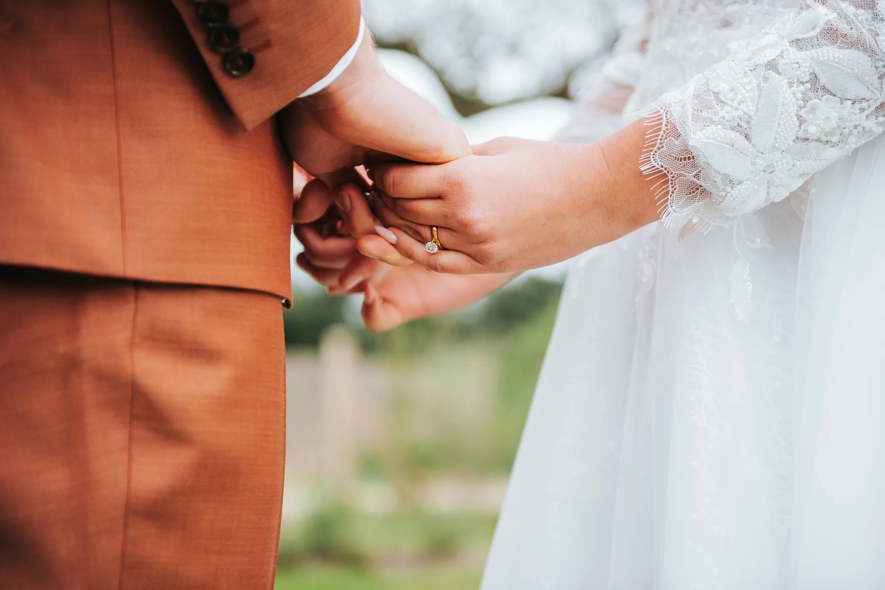 Mariage : les mains des mariés enlacées, détail de la dentelle et du costume