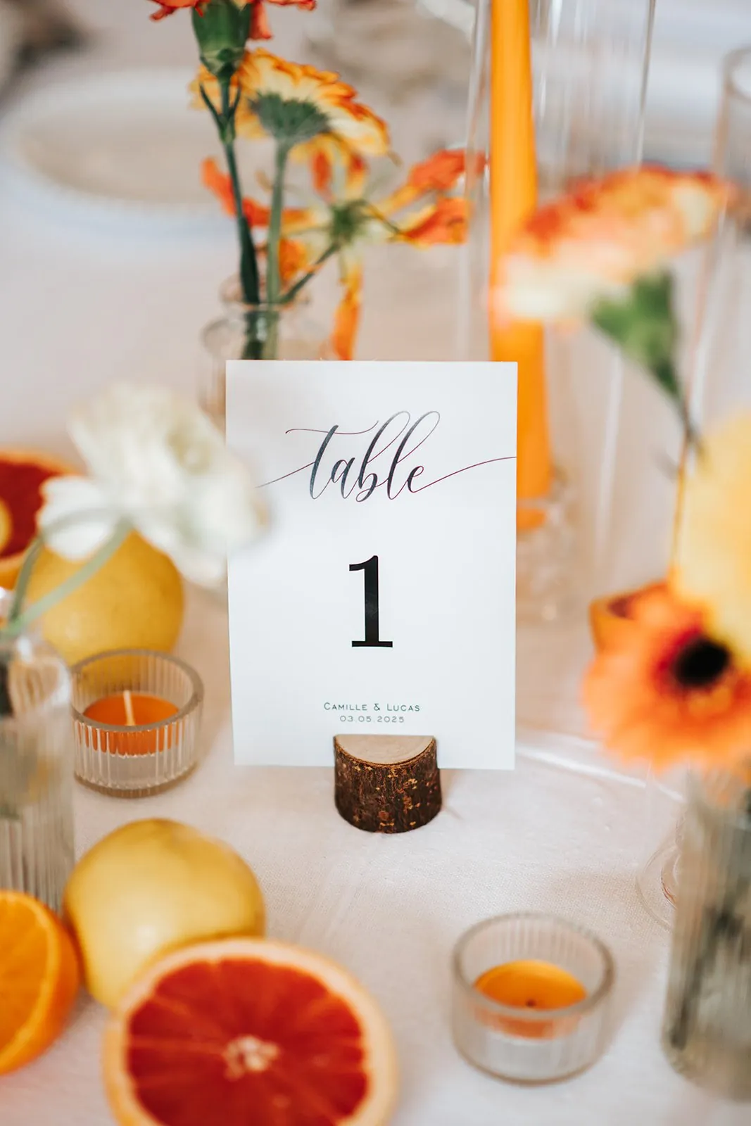 Détail de mariage : marque-place « table 1 » entouré d'agrumes, de fleurs orange et de bougies