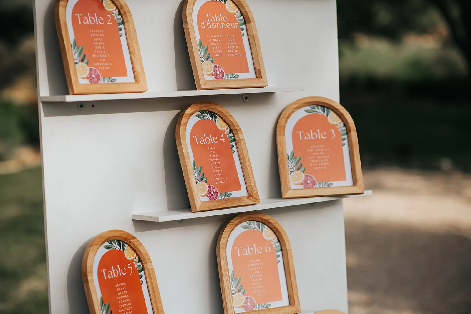 Détail de mariage : plan de table en cadres arrondis en bois, aux tons orange et agrumes