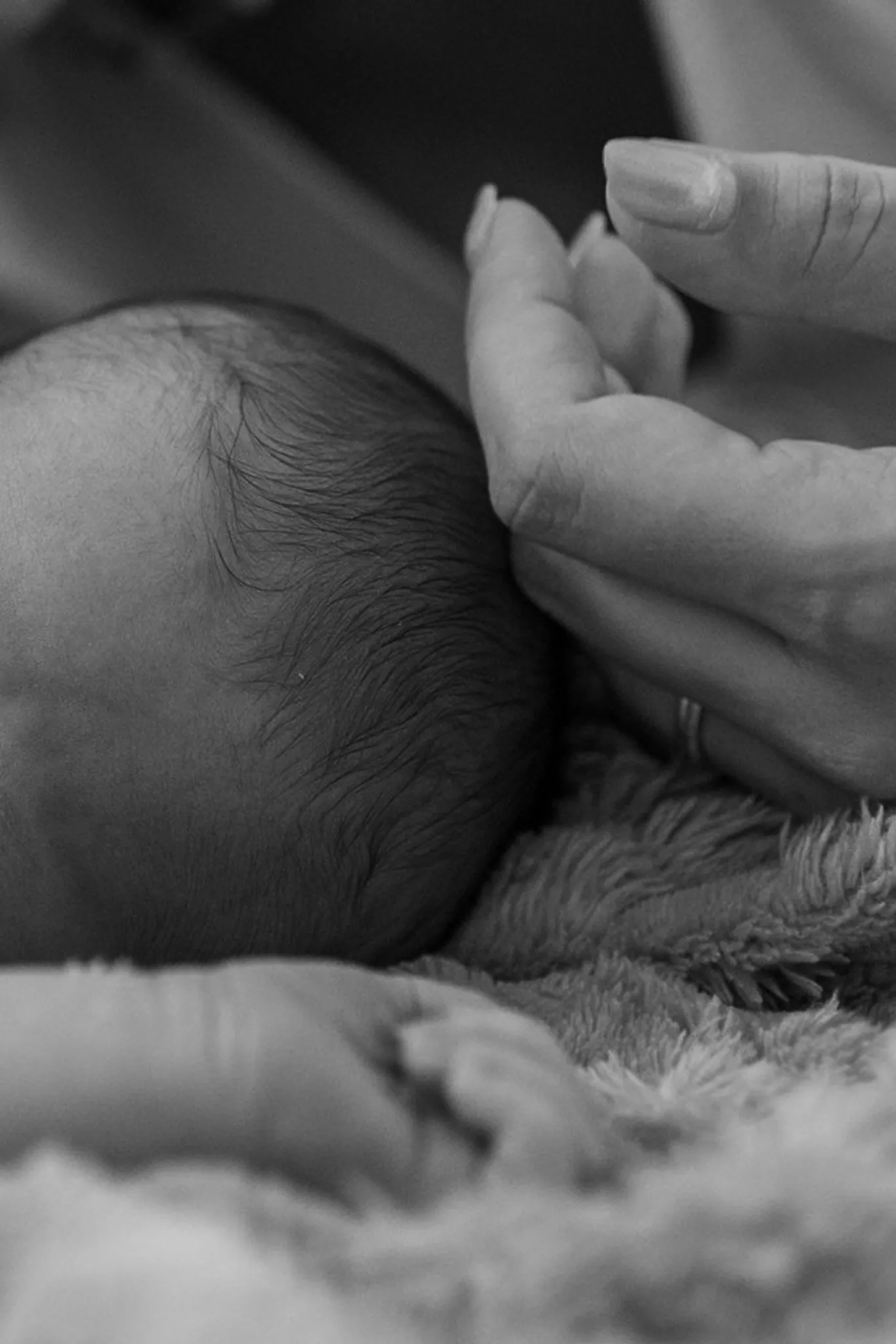 Main de maman qui effleure les fins cheveux de son nouveau-né endormi dans une couverture douce, en noir et blanc