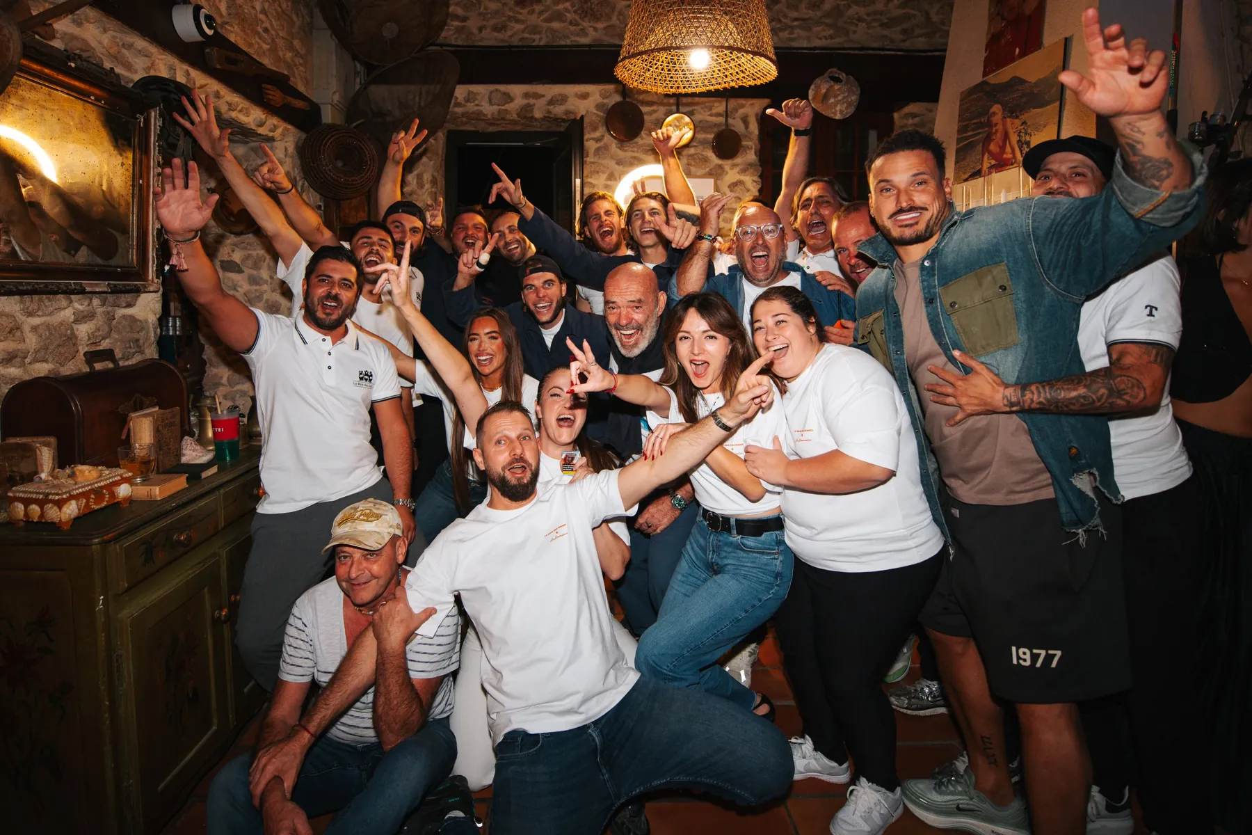 Photo de groupe d'un anniversaire : une vingtaine d'invités bras levés et grands sourires dans une salle en pierre