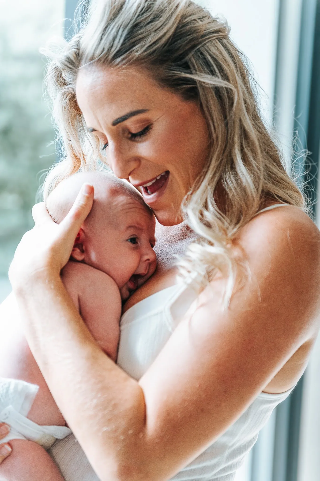 Bébé allongé sur un tissu rayé entre ses parents souriants, visages tout proches, moment complice à la maison