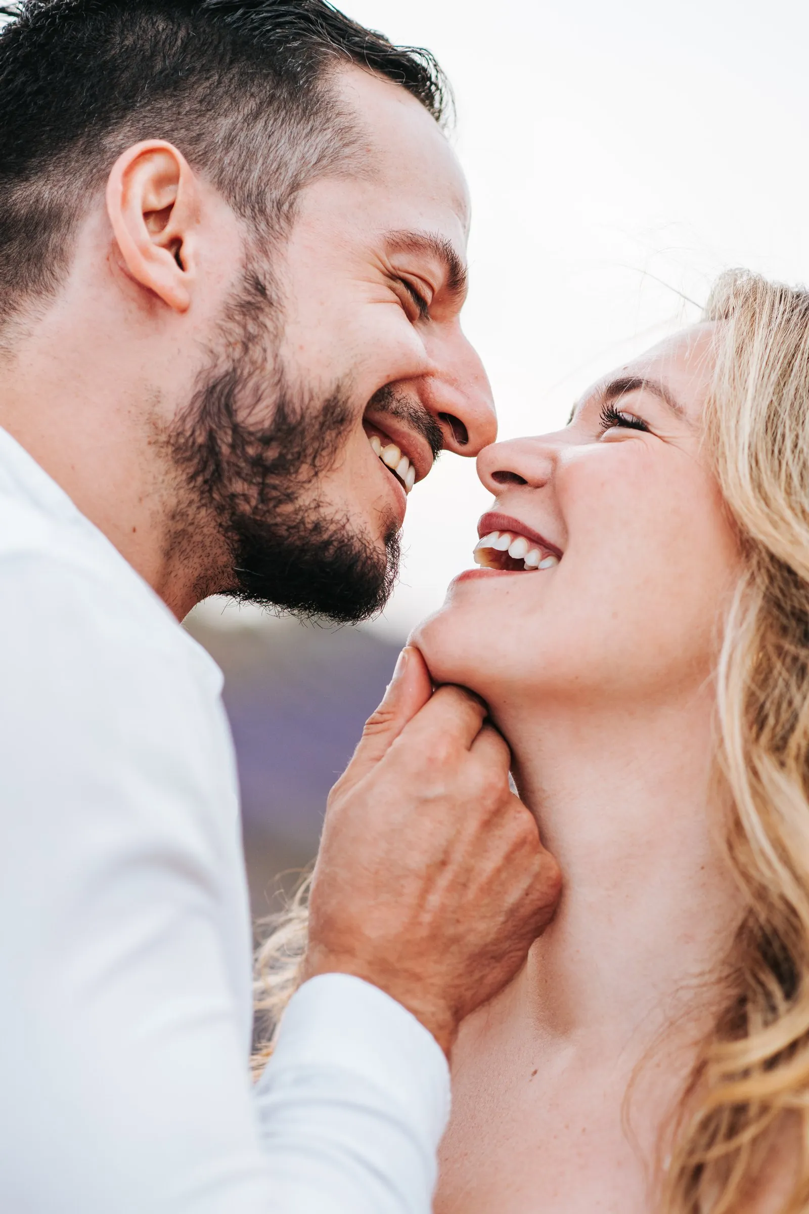 Nez contre nez, un couple éclate de rire, il lui tient doucement le menton, portrait lumineux et spontané