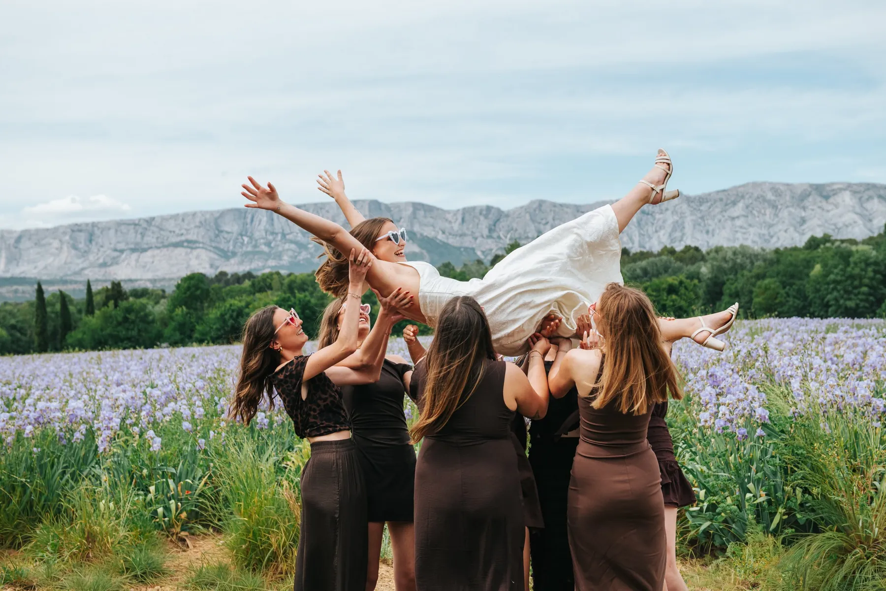 EVJF : la future mariée portée en l'air par ses amies dans un champ d'iris, au pied d'une montagne