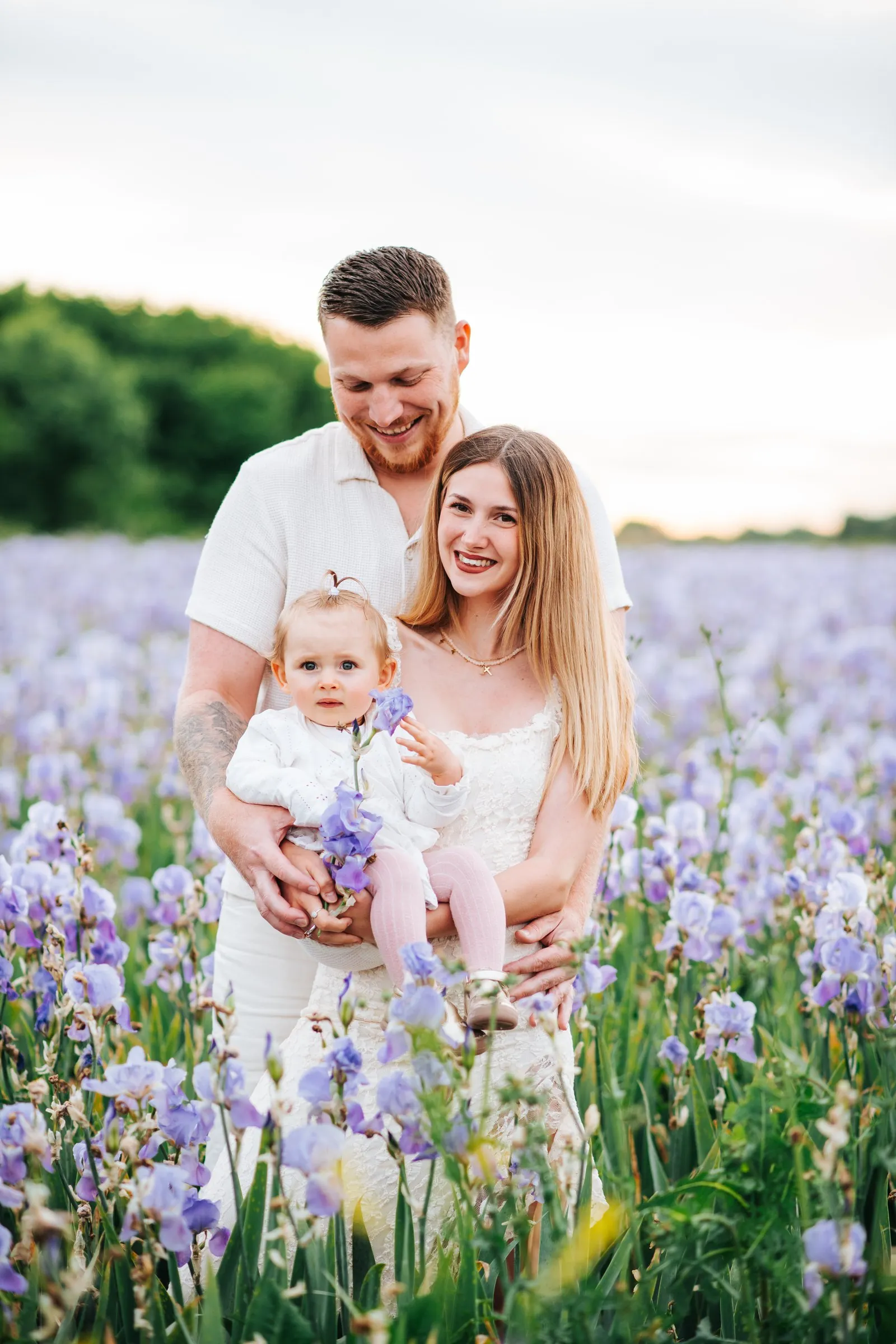 Séance famille dans les iris : les parents enlacés tiennent leur bébé qui serre une fleur violette près d'Aix-en-Provence
