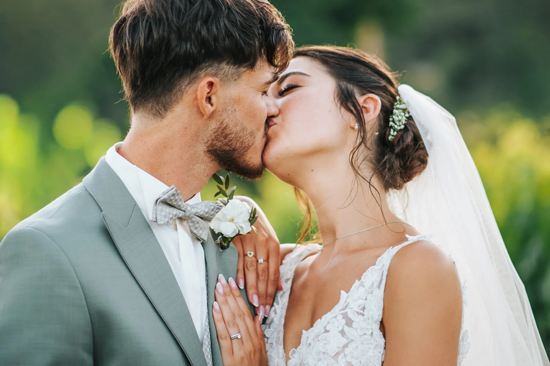 Mariage : baiser passionné des mariés, mains de la mariée posées sur le costume gris clair du marié