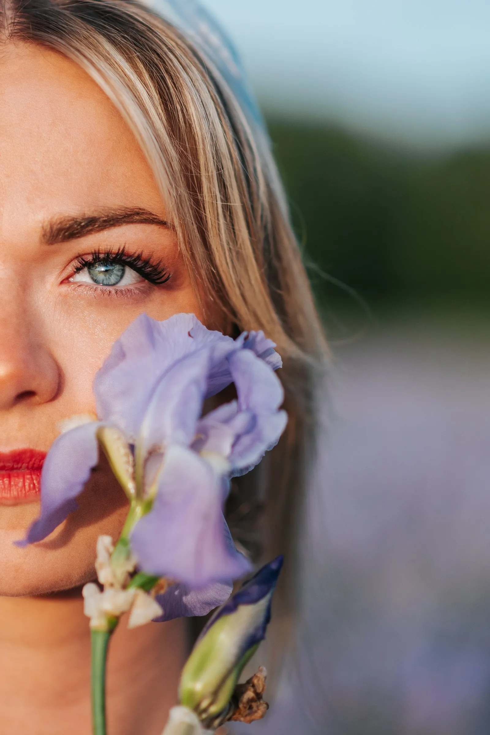 Portrait d'une femme blonde aux yeux bleus, une fleur d'iris devant le visage, lumière douce du soir, près d'Aix-en-Provence